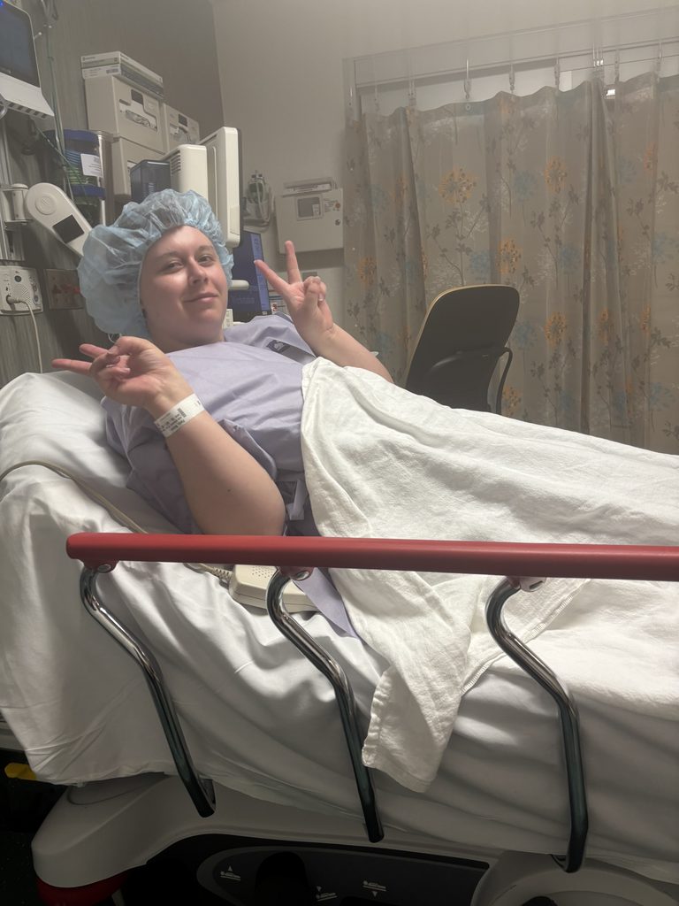 A young woman lays in a hospital bed in pre-op before surgery.